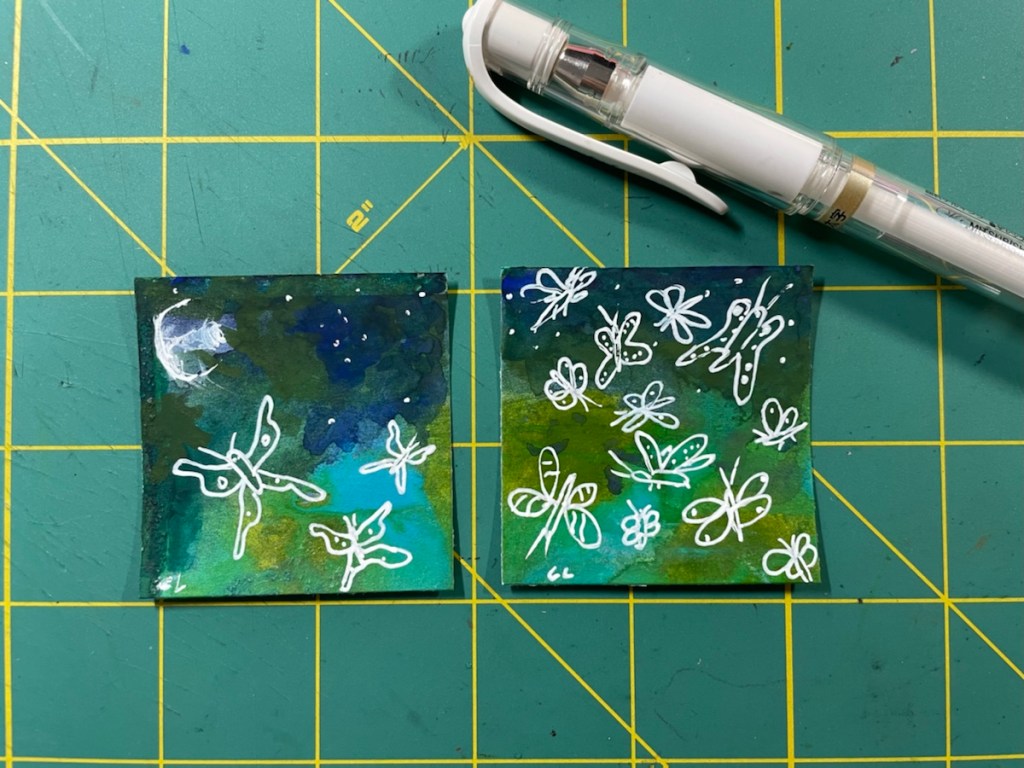 2x2 inch sized art displayed on a cutting mat to show the size.  Colors palette od blues, greens and a white gel pen was used to draw moths over the darker repainted paper.