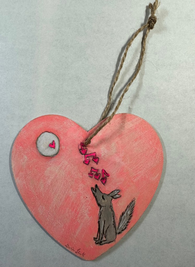 Wooden heart painted pink and distressed with a buff color. A singing coyote is portrayed with a full moon, that has a pink heart painted on it.  The coyote is singing pin musical notes that use hearts instead of circles.